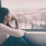 Woman sitting by window looking outside snowy landscape