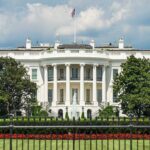 White building with columns behind a black fence.