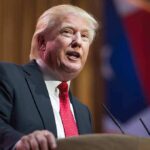 Trump’s New Strategy: Boosting Cabinet Efficiency with Team Dynamics Man in suit speaking at podium with flag background