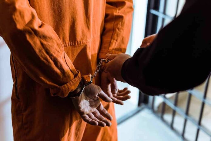 1036220185 featured image Person in orange jumpsuit handcuffed behind bars.