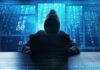 Hacker in hoodie typing on laptop with binary code.