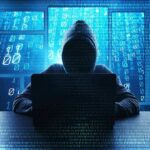 Hacker in hoodie typing on laptop with binary code.