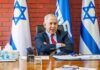 Man sitting at desk with Israeli flags behind.