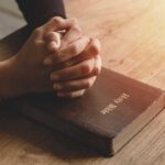Praying hands resting on a Holy Bible