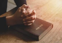 Praying hands resting on a Holy Bible