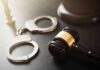Handcuffs beside a judges gavel on dark surface