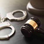Handcuffs beside a judges gavel on dark surface