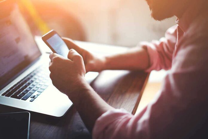 268450493 featured image Person using smartphone and laptop at desk