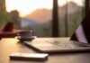Laptop, coffee cup, and phone on wooden table.
