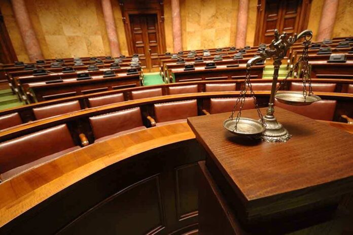 81191014 featured image Empty courtroom with scales of justice in foreground.