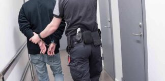 Officer escorting handcuffed person down hallway