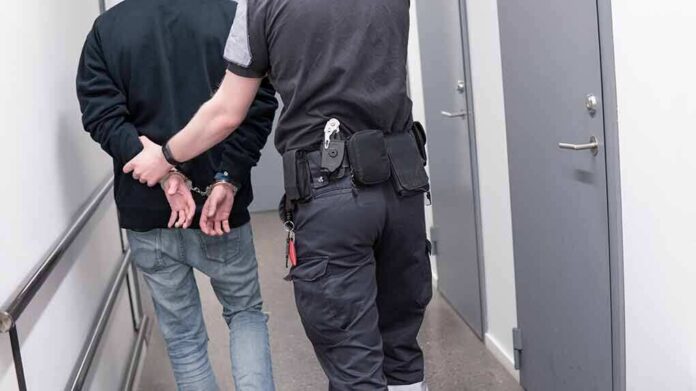 Officer escorting handcuffed person down hallway
