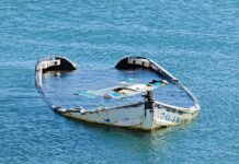 Half submerged weathered abandoned boat floating on calm water