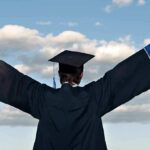 Graduate in cap and gown celebrates under cloudy sky