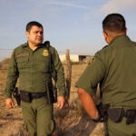 Two uniformed officers standing outdoors near a fence