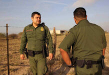 Two uniformed officers standing outdoors near a fence