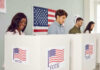 People voting in booths with American flag backdrop