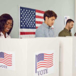 People voting in booths with American flag backdrop