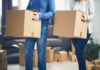 Two people carrying cardboard boxes indoors