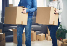 Two people carrying cardboard boxes indoors