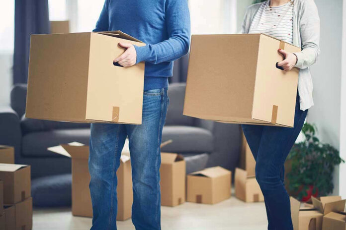 567850450 Two people carrying cardboard boxes indoors