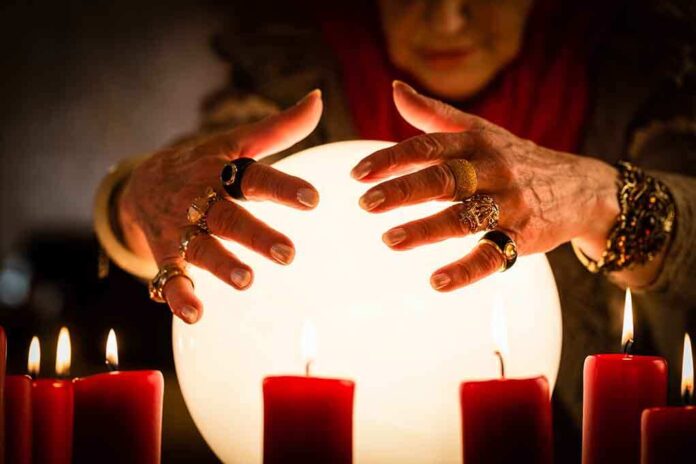 A person with adorned hands hovering over a glowing crystal ball surrounded by candles