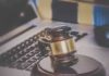 A wooden gavel resting on a desk with a laptop in the background