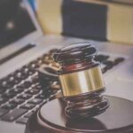 A wooden gavel resting on a desk with a laptop in the background