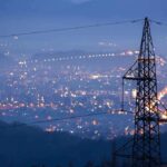 Electricity Crisis: AI Centers to Blame Night view of a city skyline with power lines in the foreground