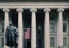 US Treasury Department building with statue and flag.