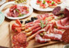 Assorted charcuterie with olives, bread, and tomatoes on plate.
