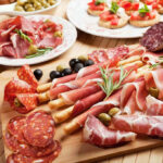 Assorted charcuterie with olives, bread, and tomatoes on plate.