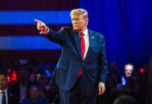Person in suit pointing during a public event.