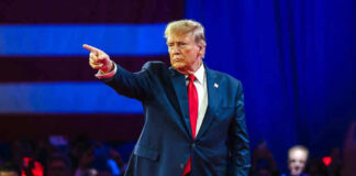 Person in suit pointing during a public event.