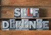 Metallic block letters spelling SELF DEFENSE on wooden shelves.