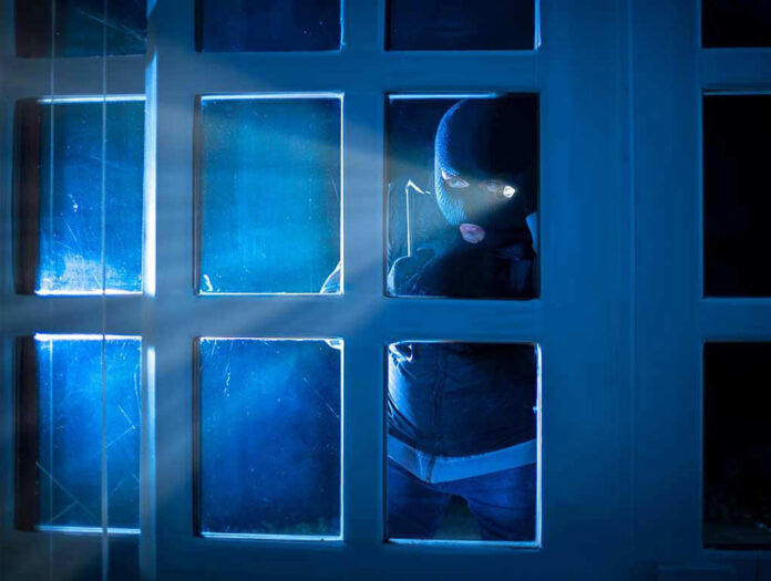 514808032 Masked figure peering through glass door at night.