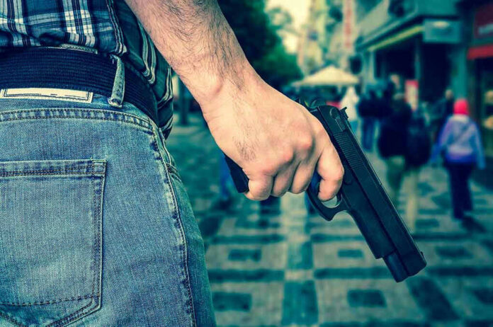 666476230 Person holding a gun in a crowded street.