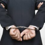 A person in a suit with hands cuffed behind their back