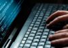 Close-up of hands typing on a laptop keyboard with code displayed on the screen