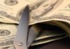 Scissors cutting through a stack of dollar bills