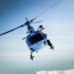A helicopter flying over a mountainous landscape under a blue sky