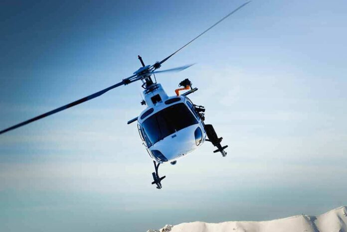 A helicopter flying over a mountainous landscape under a blue sky