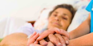A caregiver holding the hands of an elderly patient in a hospital bed