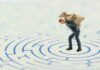A miniature businessman carrying a sack labeled DEBT in a maze