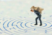 A miniature businessman carrying a sack labeled DEBT in a maze