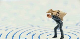 A miniature businessman carrying a sack labeled DEBT in a maze