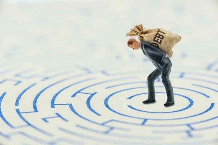 A miniature businessman carrying a sack labeled DEBT in a maze