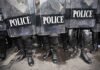Police officers in riot gear standing behind shields marked POLICE