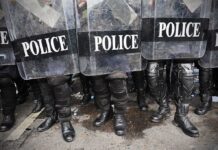 Police officers in riot gear standing behind shields marked POLICE
