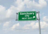 Sanctuary Laws Shield KILLER — County Leader DEAD Green road sign saying sanctuary city next exit
